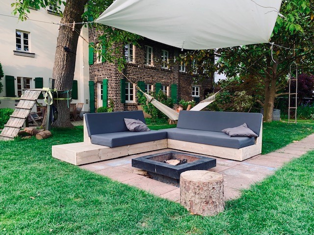 Een loungemeubel met zwarte kussens van steigerhout in Venlo in een tuin.